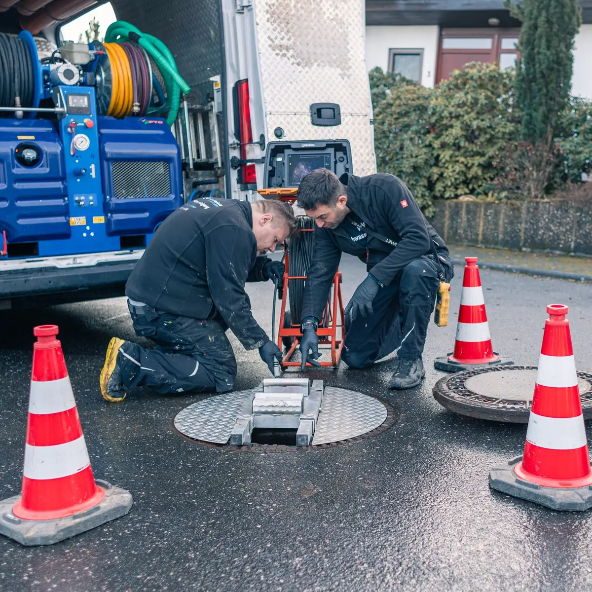 Zwei Techniker am geöffneten Kanalschacht vor dem Spülfahrzeug